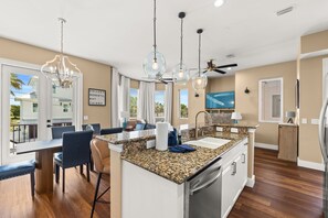 A modern kitchen with a central island, pendant lights, and a dining area with chairs. - Fully Renovated 5 BDR PCB House-Walk to Beach! (Panama City Beach)