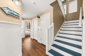 A hallway with a staircase, white doors, and a sign that reads 'To the Beach.' - Fully Renovated 5 BDR PCB House-Walk to Beach! (Panama City Beach)