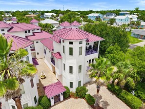 A multi-story building with a central courtyard, surrounded by lush greenery and palm trees. - Fully Renovated 5 BDR PCB House-Walk to Beach! (Panama City Beach)