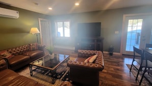 Uma sala de estar com sofá em formato de L, uma mesa de centro de vidro, uma televisão e um espaço de jantar com mesa e cadeiras.