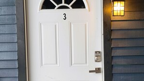 Uma porta branca com o número 3, um olho-mágico, um toque de campainha e uma luminária fixada na parede.