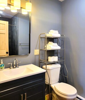 Een badkamer met een wit wastafelmeubel, een spiegel, een toilet en een metalen plank met handdoeken.
