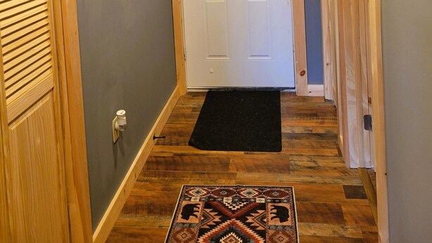 Un pasillo con una puerta de madera, un felpudo negro y una lámpara de pared.