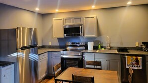 Una cocina moderna con electrodomésticos de acero inoxidable, muebles grises y una mesa de comedor de madera.