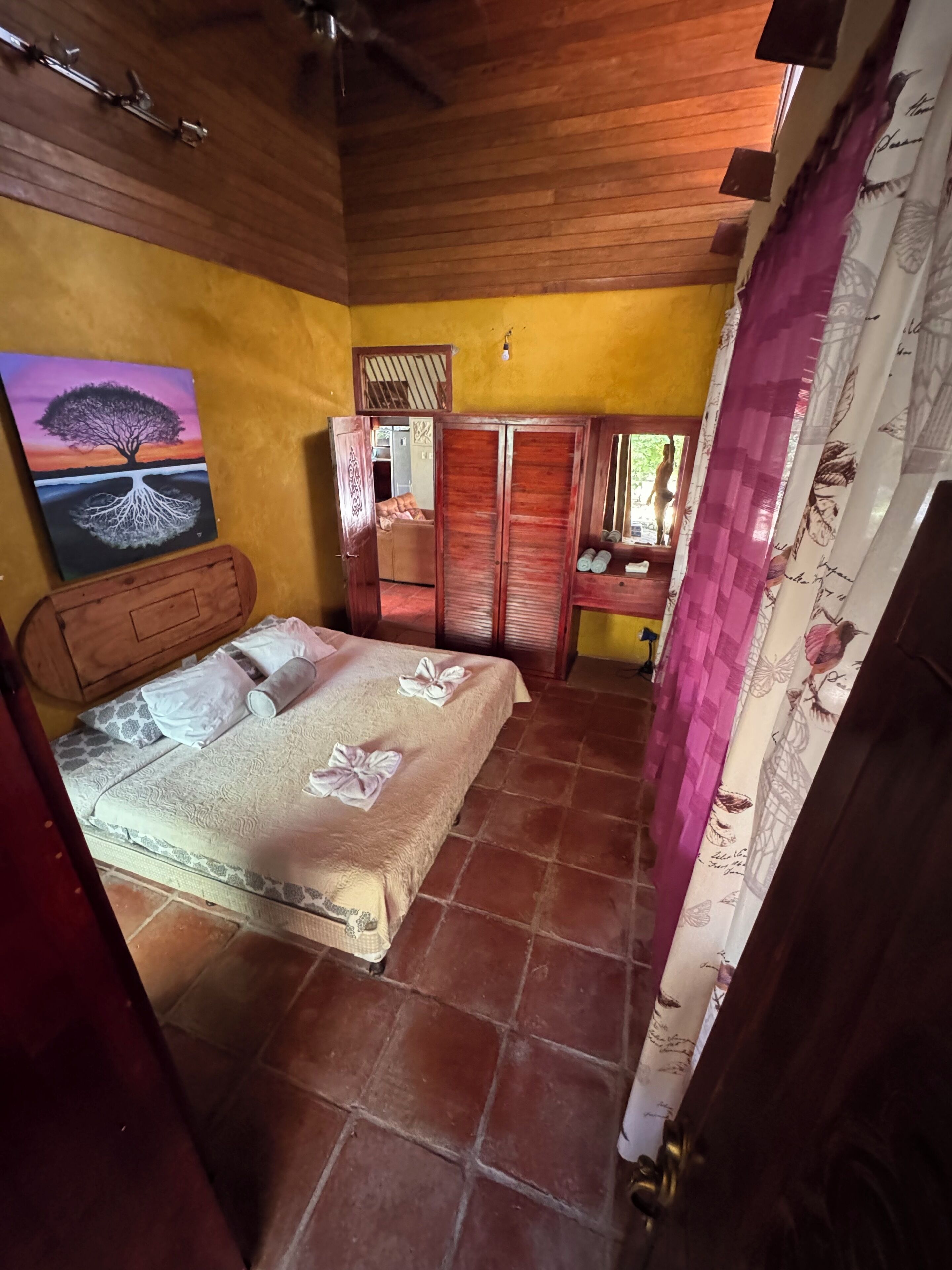 A bedroom with a bed, wooden wardrobe, and a painting on the wall.