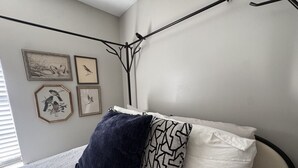 A bedroom with a bed, a black metal headboard, and wall-mounted artwork.