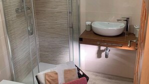 A bathroom with a glass-enclosed shower, a white sink, and a round mirror.