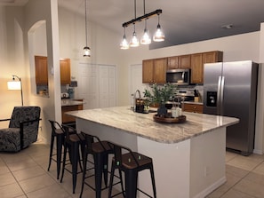 A modern kitchen with a central island, bar stools, wooden cabinets, stainless steel appliances, and pendant lighting. - Spacious 4-bedroom and two bathroom house in tranquil Port St. Lucie  (Port St. Lucie)