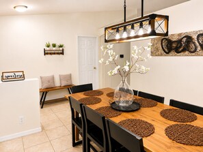 A dining area with a wooden table, black chairs, and a hanging light fixture.
