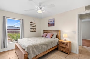 A bedroom with a bed, a bedside table with a lamp, a ceiling fan, a window with curtains, and a wall-mounted shelf. - Spacious 4-bedroom and two bathroom house in tranquil Port St. Lucie  (Port St. Lucie)