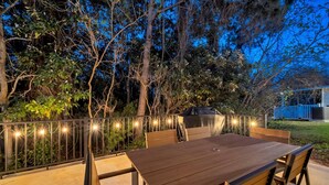 Een terras buiten met een houten tafel en stoelen, omringd door een metalen hek en lichtslingers.