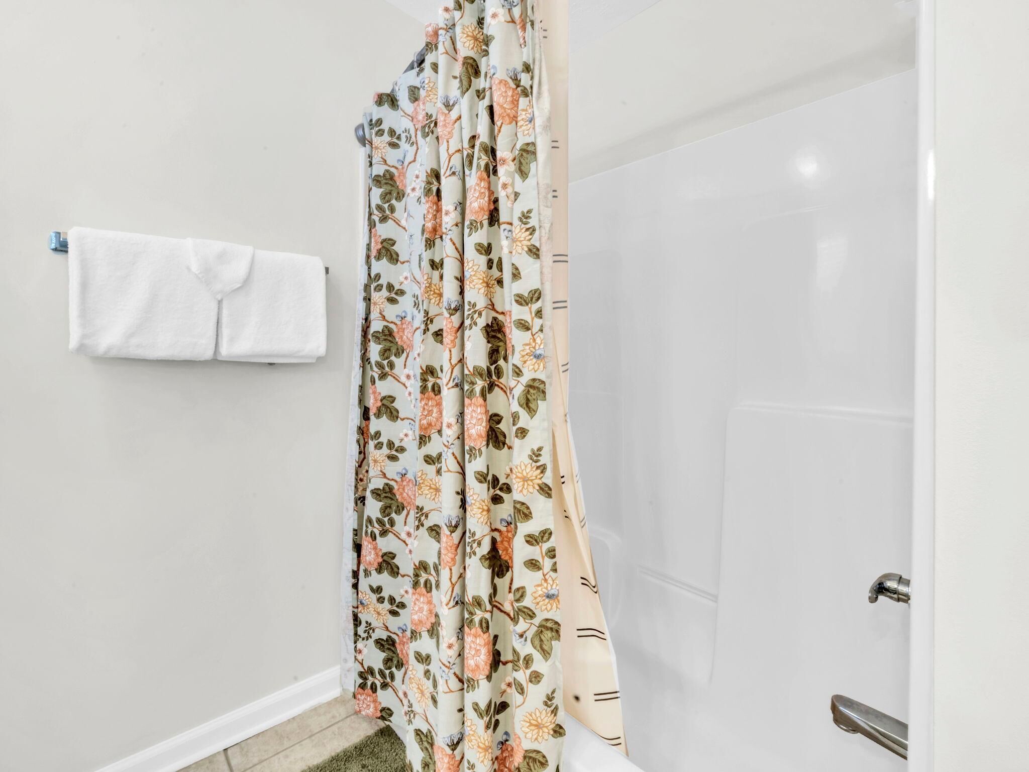 Un baño con cortina de ducha estampada con motivos florales, una toalla blanca colgada en la pared y cabezal de ducha visible.