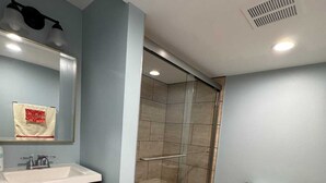 Un baño moderno con cabina de ducha de vidrio, inodoro, lavamanos con espejo y muebles de madera oscura.