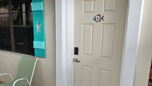 A white door with a small decorative sticker, a green chair, and a black doormat on a wooden deck. - 213 Deluxe Single Room in a waterfront hotel in Singer Island, FL (Riviera Beach)