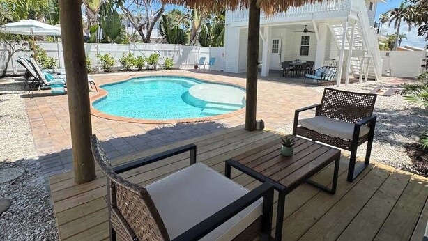 A covered outdoor area with a pool, wooden deck, and seating. - Beach Bungalow- 2 min walk to beach! Heated Pool (Bradenton Beach)