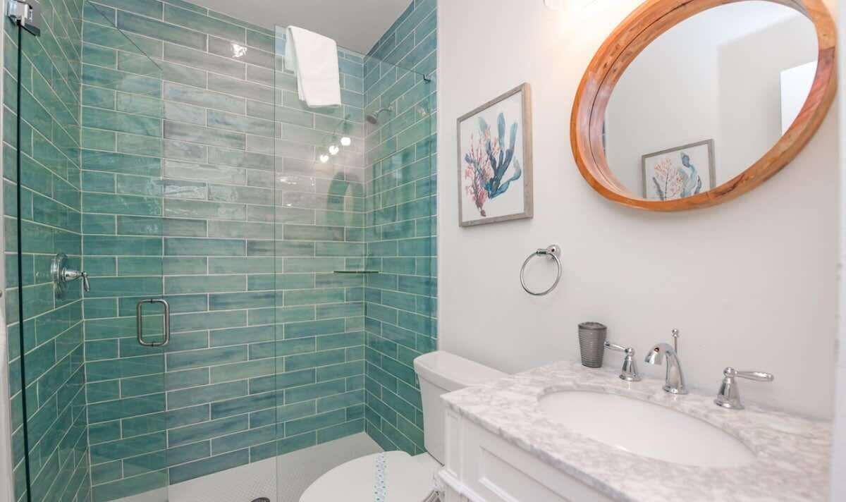 Een badkamer met een douchecabine van glas, een wit wastafelmeubel met een marmeren blad en een spiegel met houten lijst.