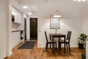 A compact kitchen with modern appliances, a dining area with a table and chairs, and a dark door in the background. - New built and stylish apartment in Barkarbystaden (Järfälla)