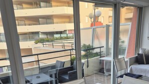 Uma varanda com mesa, cadeiras, um sofá e vista para um prédio na rua.