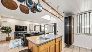 Una cocina moderna con una isla central, un comedor con sofá y una sala de estar con televisor.