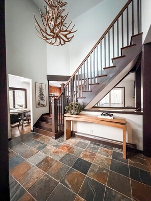 Ein modernes Interieur mit einer Holztreppe, einem Kronleuchter und einem Essbereich mit Blick.