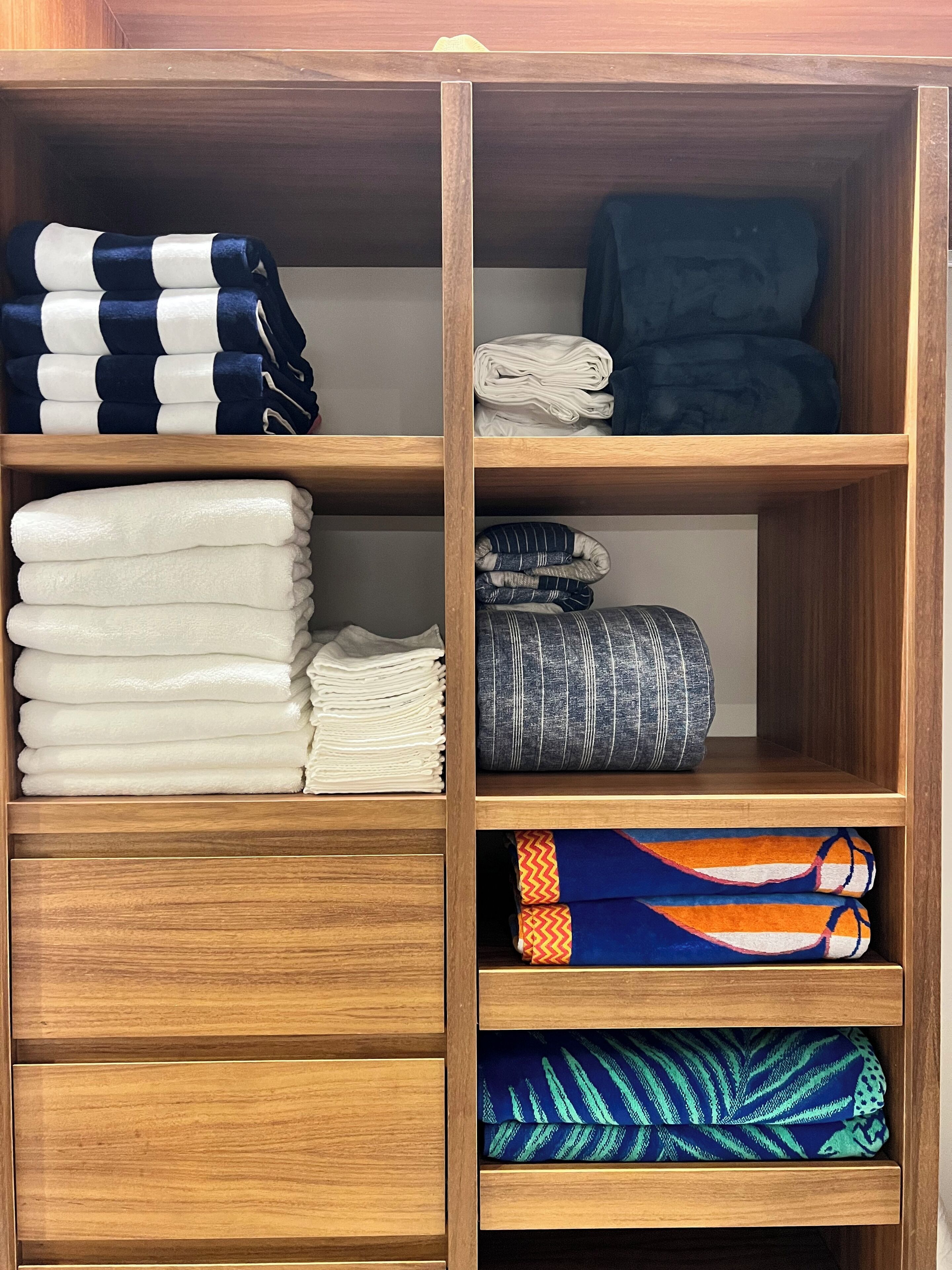 A wooden wardrobe with multiple shelves, each containing folded towels and blankets in various colors and patterns.
