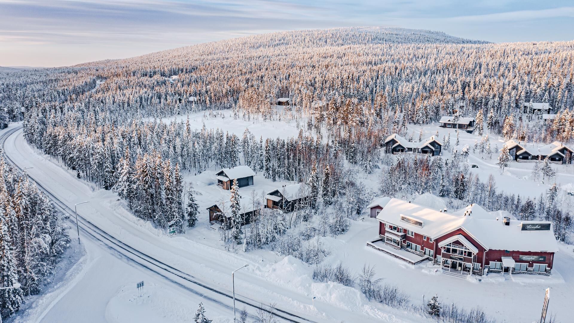A snow-covered landscape with multiple cabins and a main lodge, surrounded by dense forests.