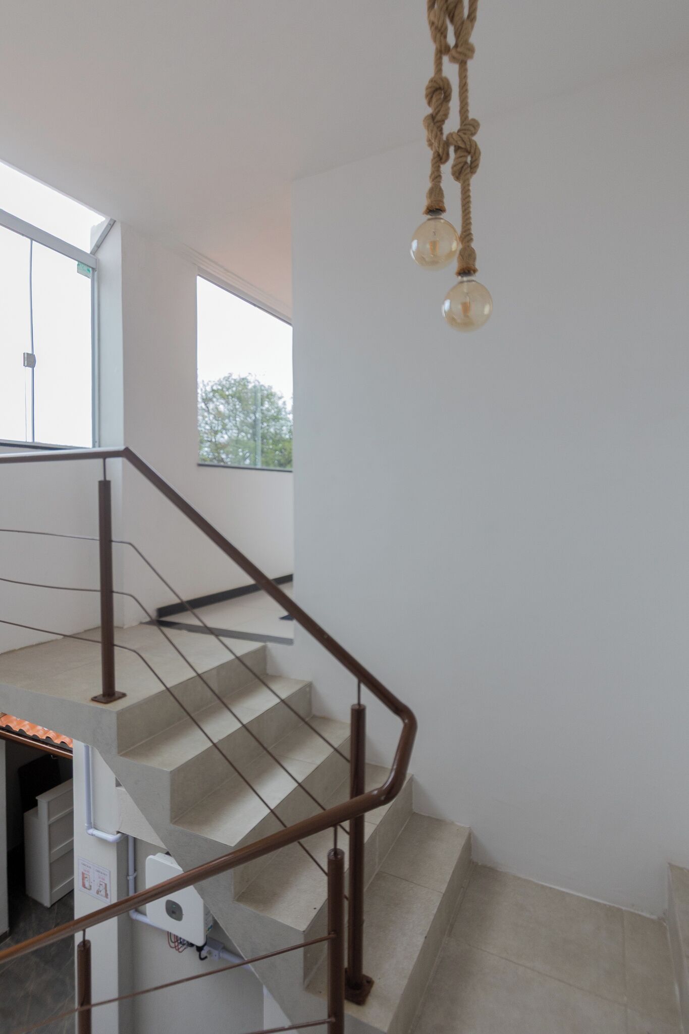 Um interior moderno com escada, luminária pendente e vista para o exterior.