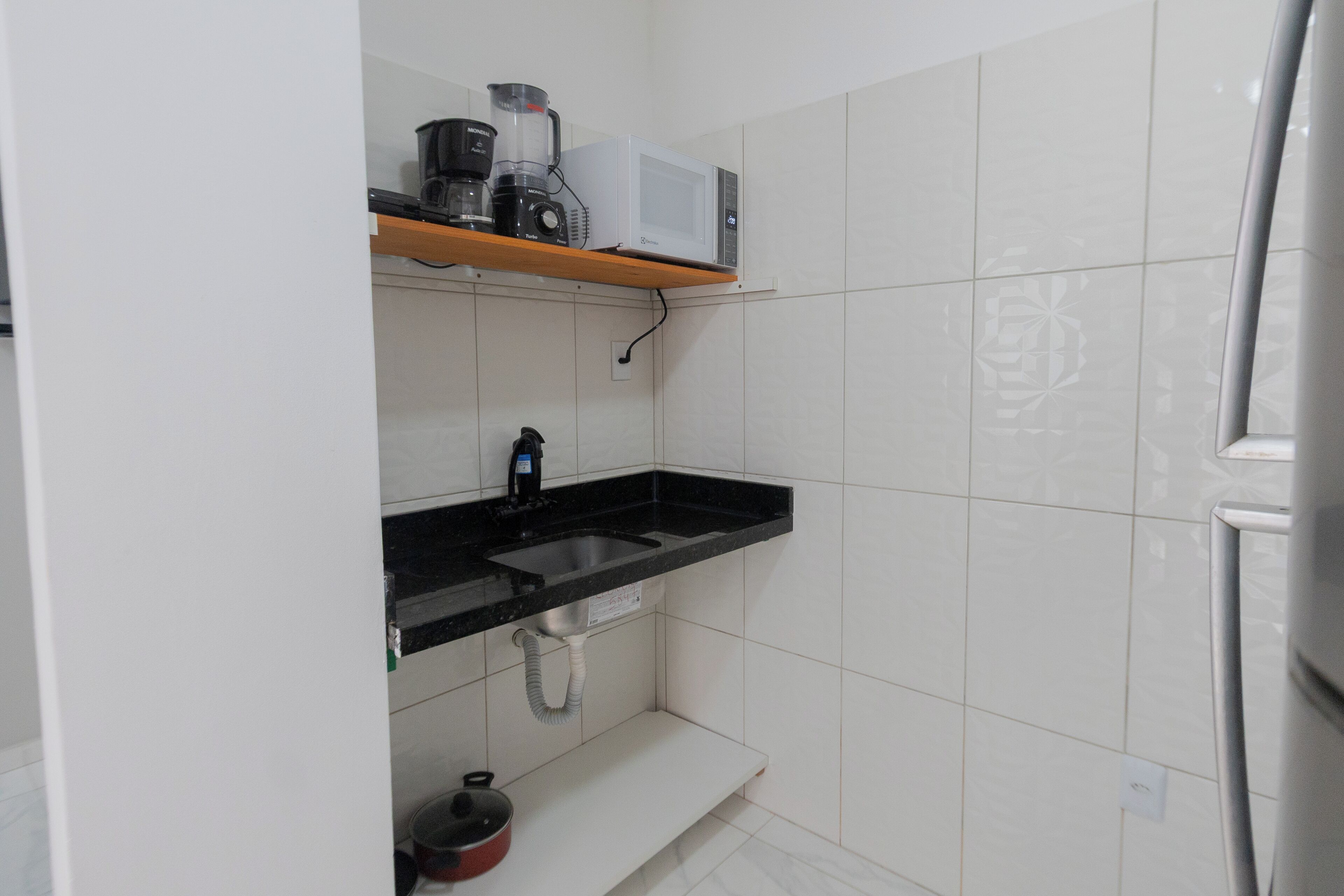 A kitchen with a black countertop, a stainless steel sink, and a white tiled backsplash.