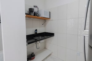 Una cocina con encimera negra, pileta de acero inoxidable y salpicadero blanco de azulejos.
