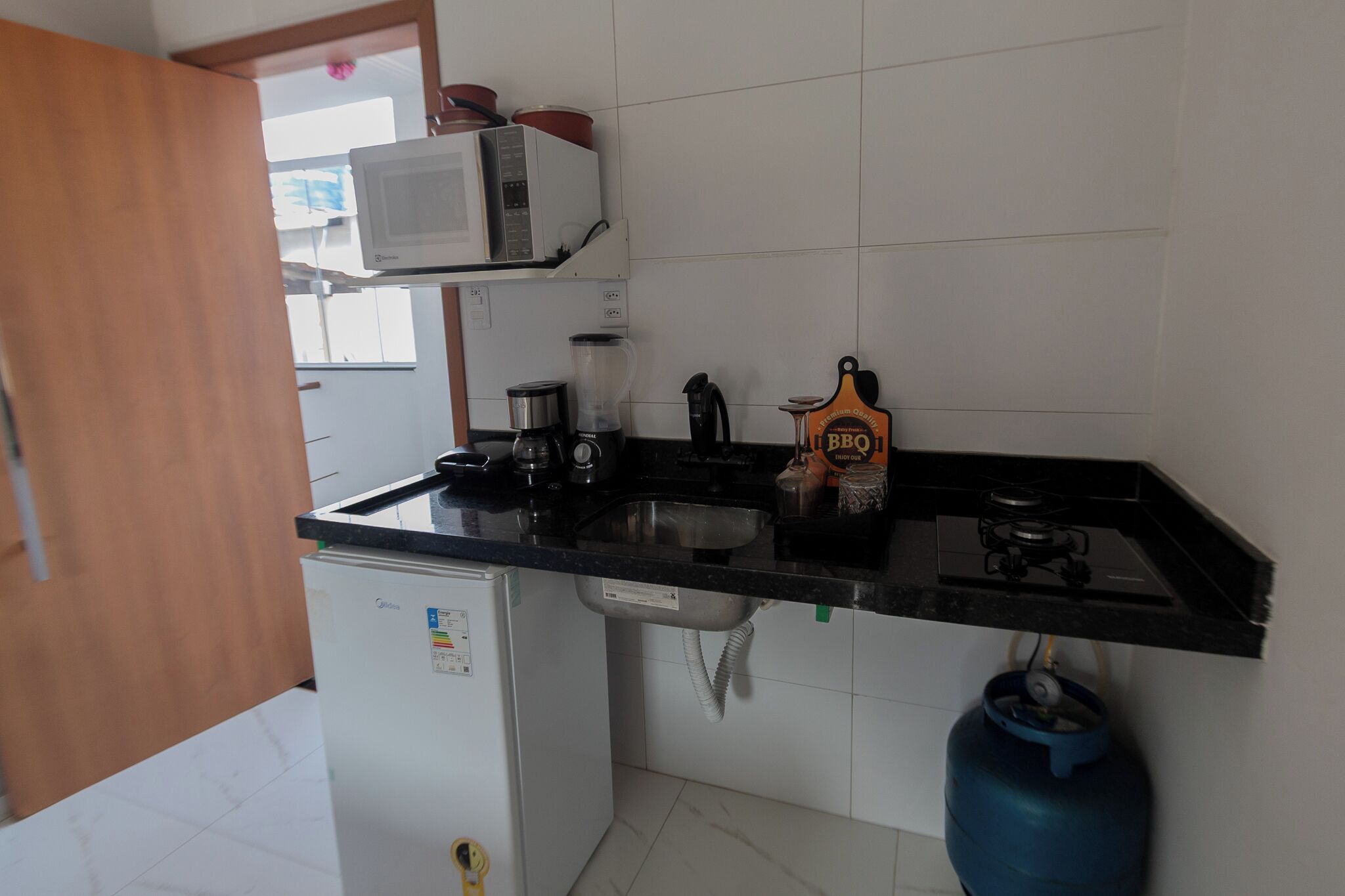 Cozinha compacta com micro-ondas, liquidificador, chaleira e fogão a gás.