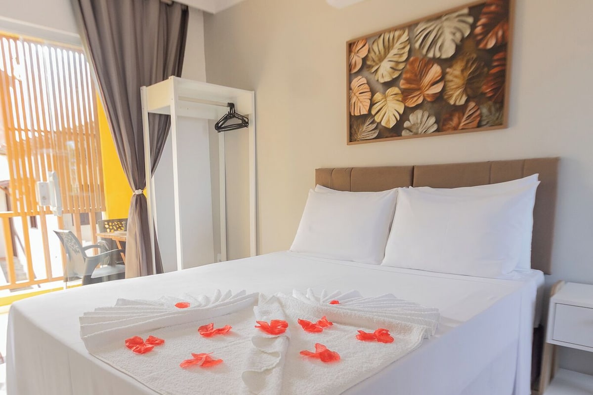 Ein Hotelzimmer mit einem Bett, weißen Bettwäsche, einem Gemälde und einem Fenster mit Vorhängen.