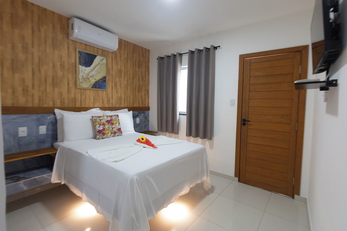 Ein Hotelzimmer mit einem Bett, einem Holz-Kopfteil, einer Wand-Klimaanlage, einer Tür und einem Fenster mit Vorhängen.