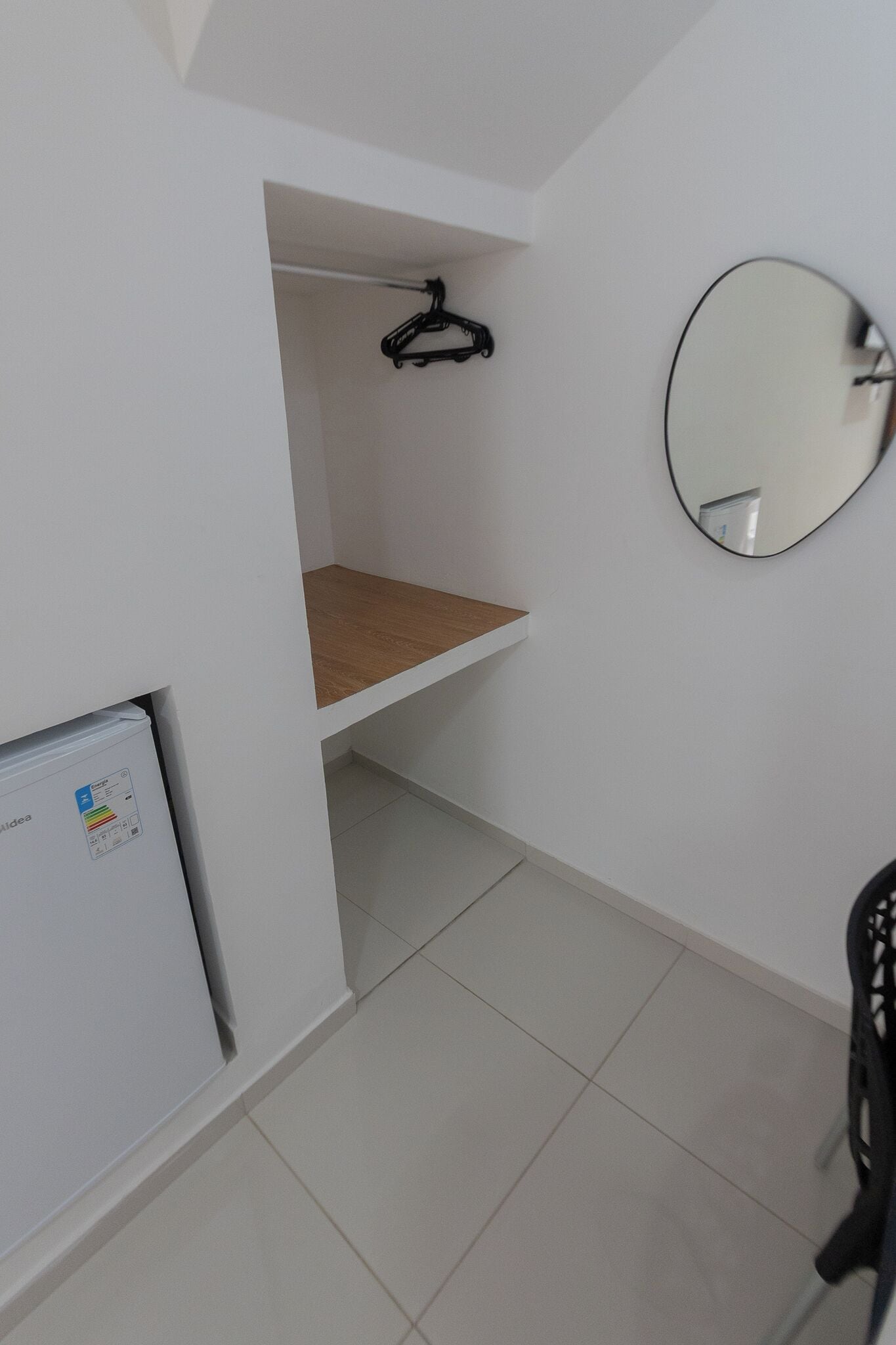 Quarto com parede branca, espelho, cabide preto, armário branco e chão com azulejos.
