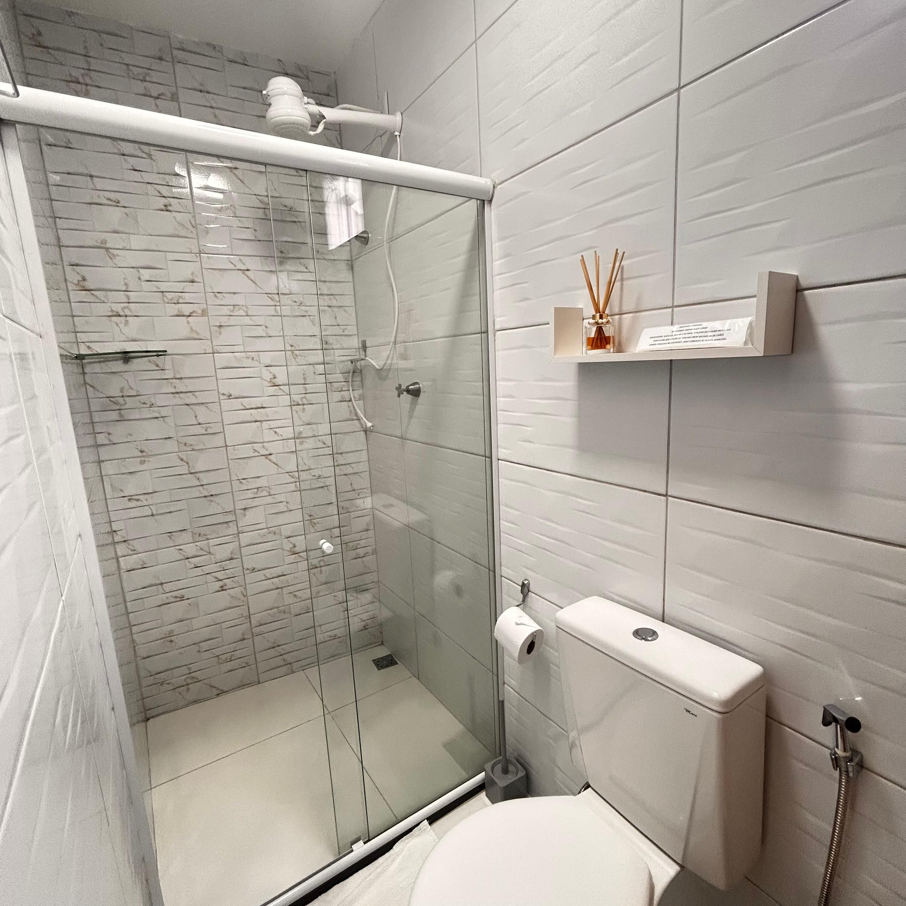 A modern bathroom with a glass-enclosed shower, a toilet, and a shelf with a bottle of reed diffuser.
