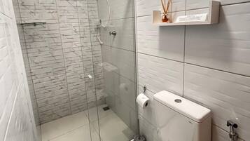 A modern bathroom with a glass-enclosed shower, a toilet, and a shelf with a bottle of reed diffuser.