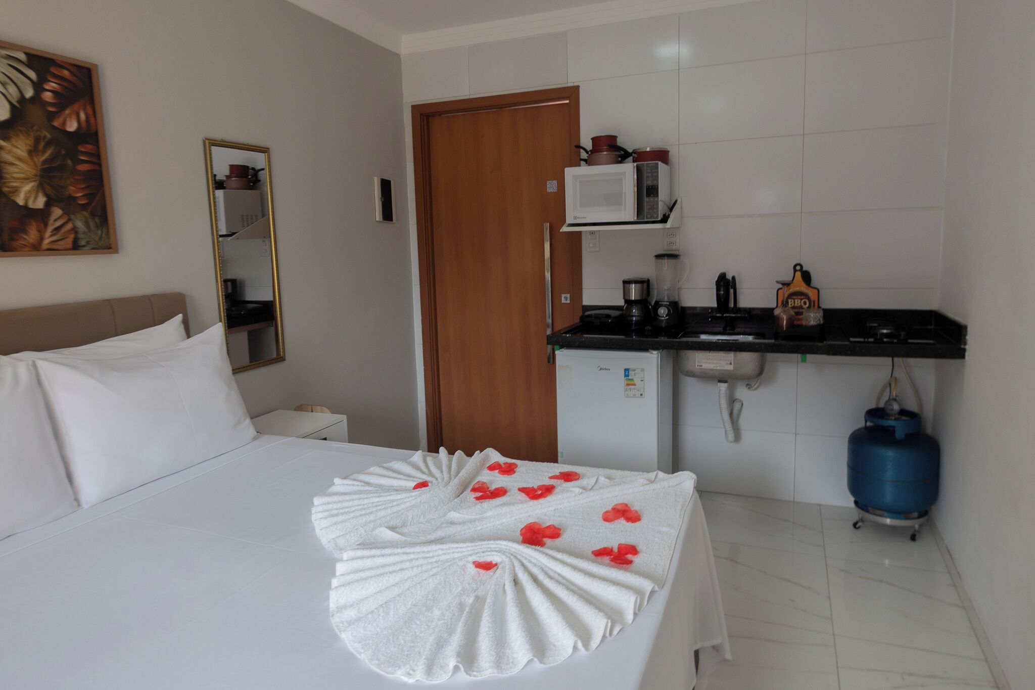 Habitación de hotel con cama, kitchenette pequeño, microondas, cafetera y cilindro de gas azul.