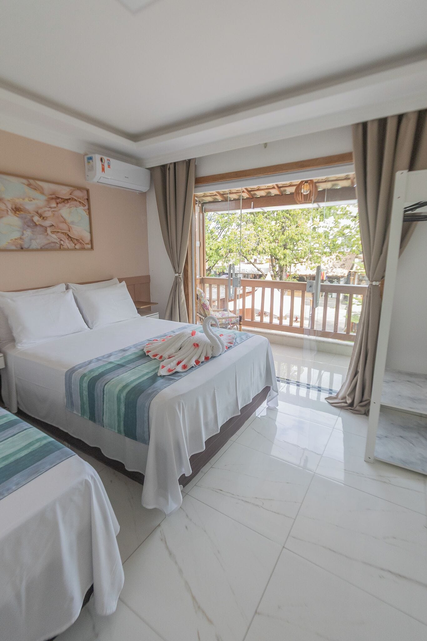 Habitación de hotel con cama, una mesita, una silla y un balcón con vistas a árboles y una cerca.