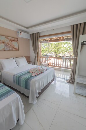 Habitación de hotel con cama, una mesita, una silla y un balcón con vistas a árboles y una cerca.