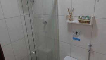 Un baño con cabina de ducha de vidrio, inodoro y repisa con artículos de aseo.