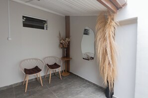 Una habitación con dos sillas de estructura metálica, una mesita con un jarrón de flores secas y un espejo grande en la pared.