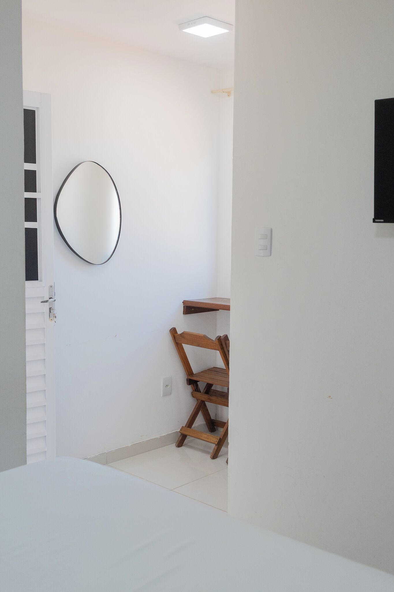 A room with a white door, a wooden chair, a small wooden table, and a wall-mounted mirror.
