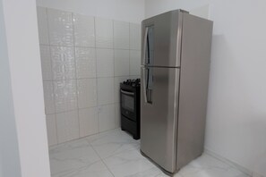 A kitchen with a stainless steel refrigerator, a stove, and patterned tiles on the wall.