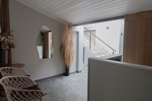Un intérieur moderne avec un escalier, une grande plante et un coin salon avec des fauteuils.