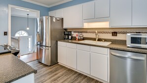 A modern kitchen with white cabinets, stainless steel appliances, a granite countertop, and a view to the living area.