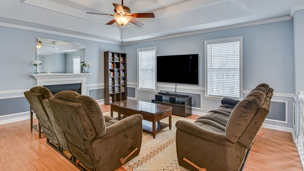 A living room with a fireplace, a ceiling fan, a flat-screen TV, and a bookshelf.