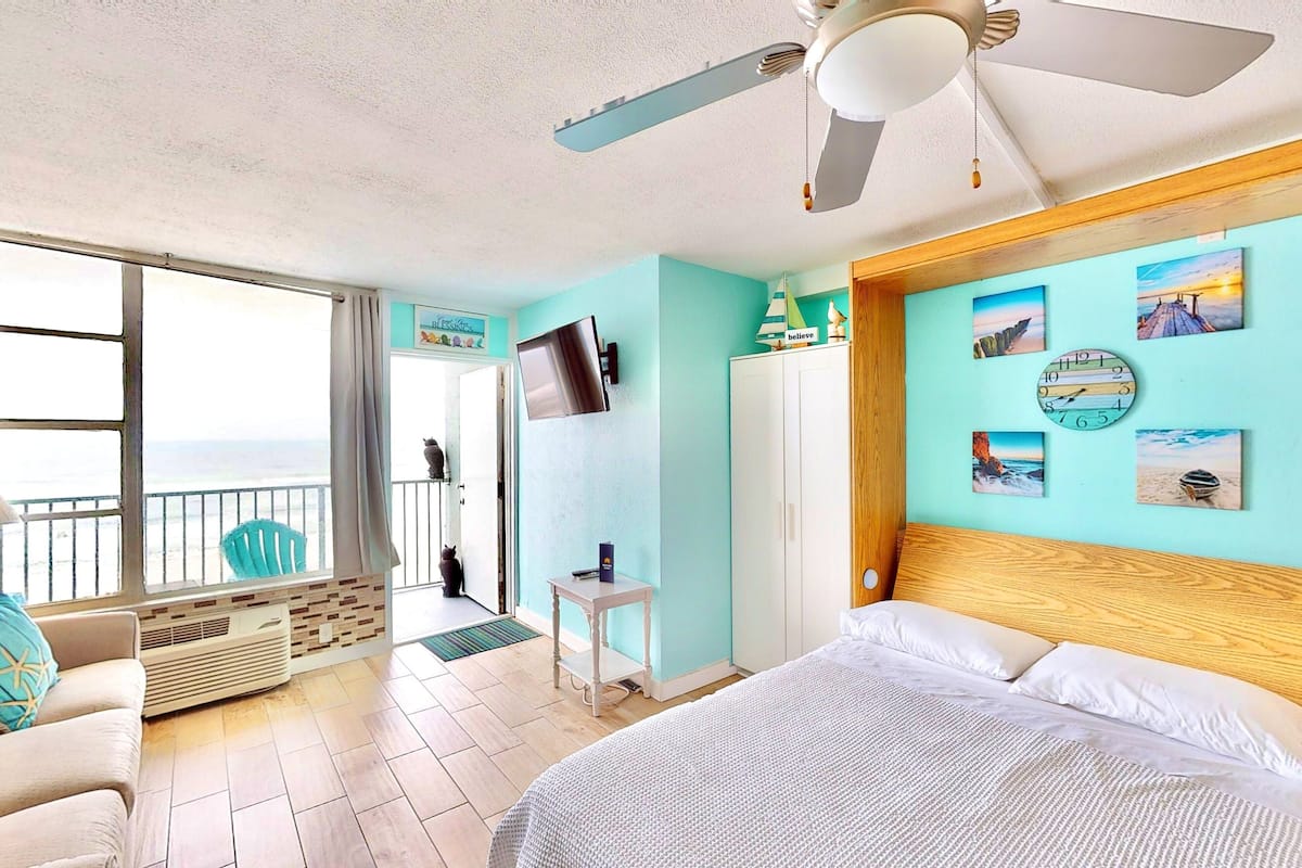 A bedroom with a bed, a ceiling fan, a TV, and artwork on the walls.