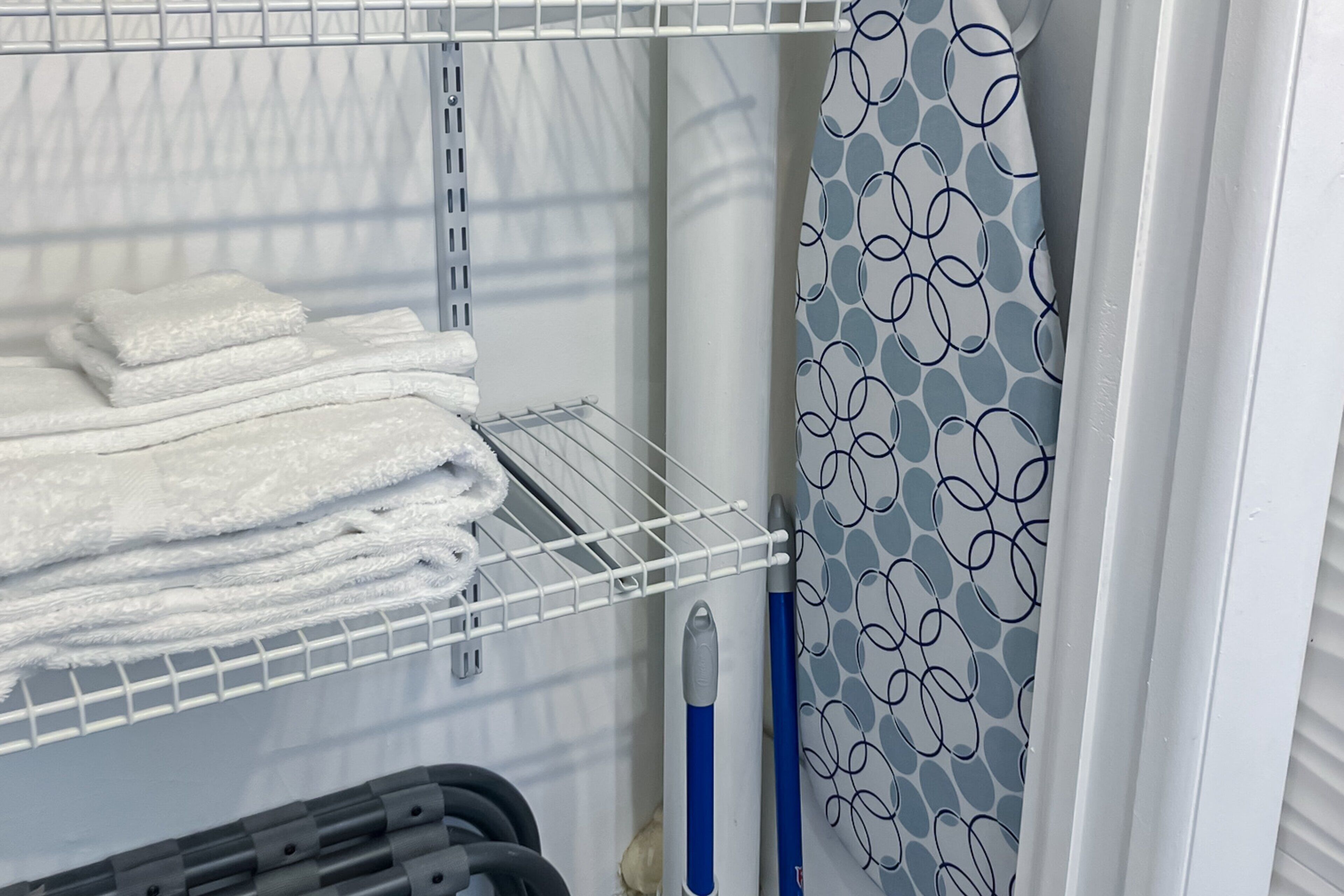 A neatly organized storage area with folded towels, a metal drying rack, and cleaning supplies.