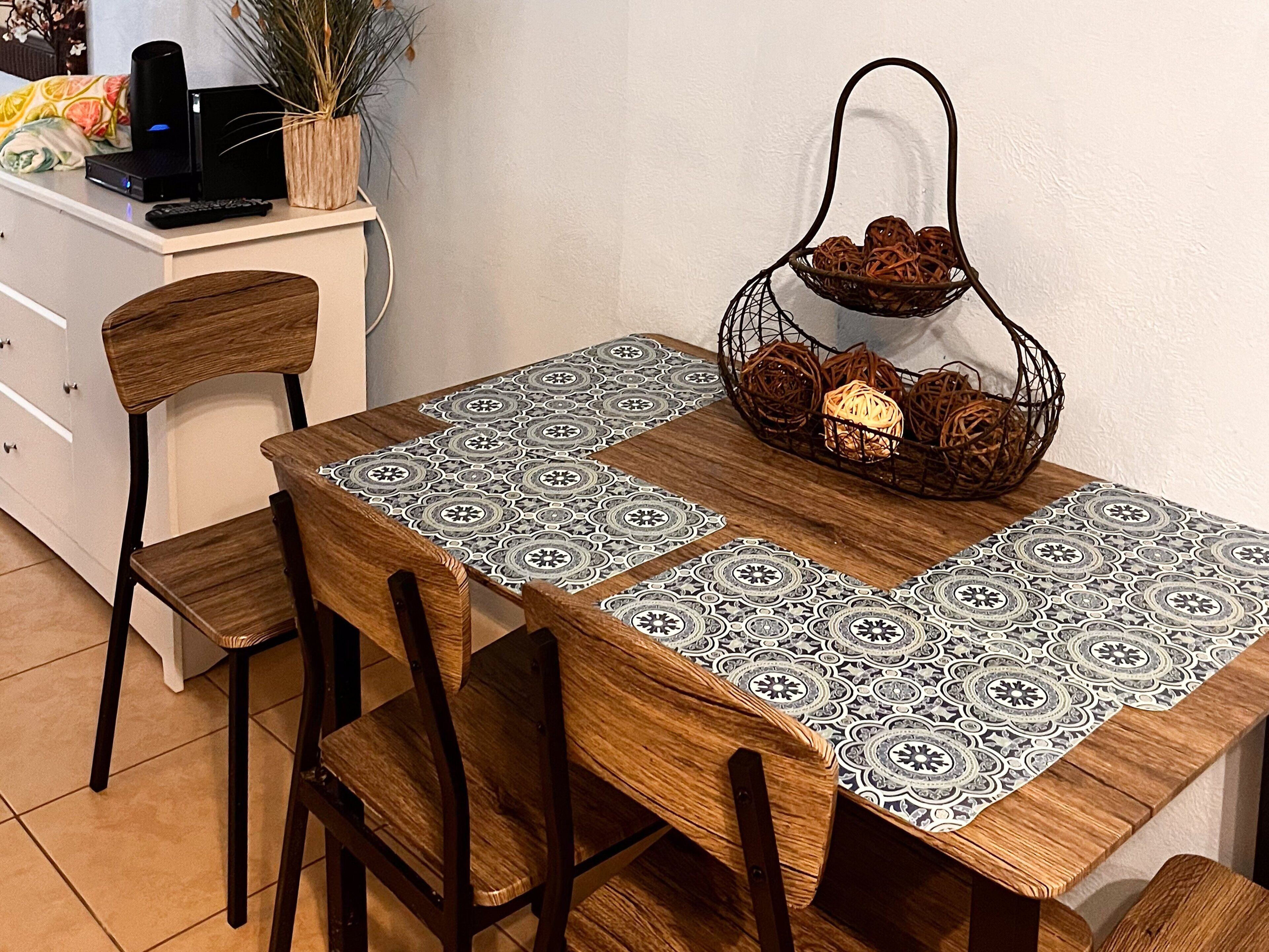 A dining table with a patterned tablecloth, wooden chairs, and a decorative basket with candles.