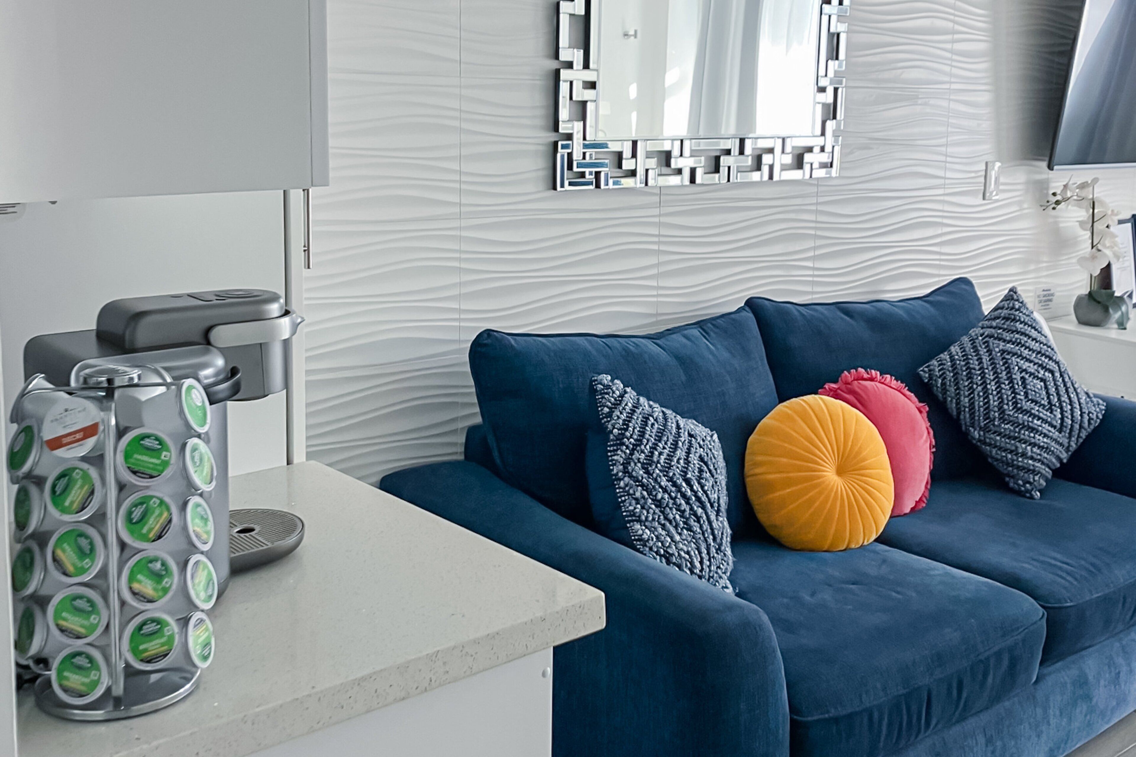A modern living room with a blue sofa, a coffee machine, and a decorative mirror.