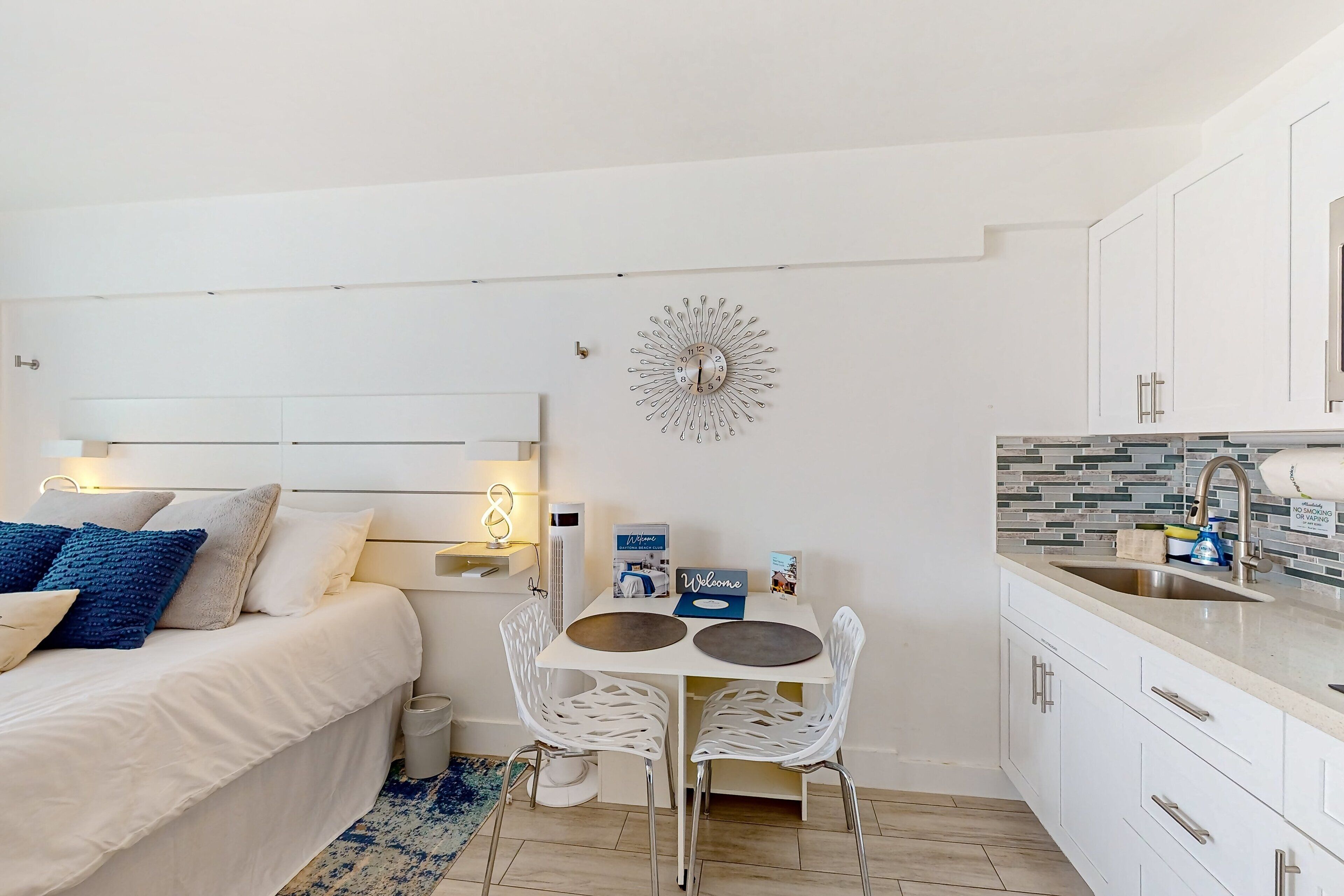 A compact bedroom with a bed, bedside table, and a small dining area with a table and chairs.